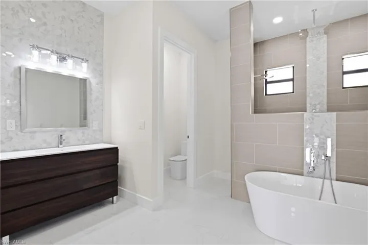 Full bath with tile walls, vanity, a freestanding bath, light marble finish floors, and tiled shower