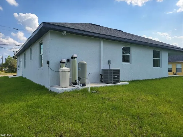 Rear view of property featuring central AC unit and a lawn