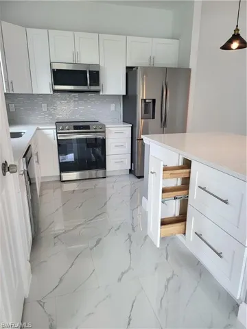 Kitchen featuring hanging light fixtures, decorative backsplash, stainless steel appliances, and white cabinets