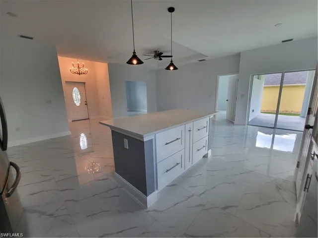 Kitchen featuring hanging light fixtures, a center island, ceiling fan with notable chandelier, and white cabinets