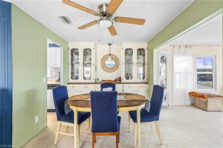 Dining space featuring light carpet, wooden walls, and a ceiling fan