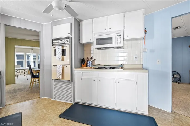 Kitchen with white cabinets, light countertops, light colored carpet, wooden walls, and white microwave