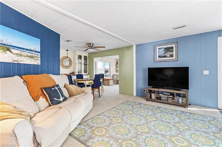 Living area featuring carpet flooring, wood walls, and a ceiling fan