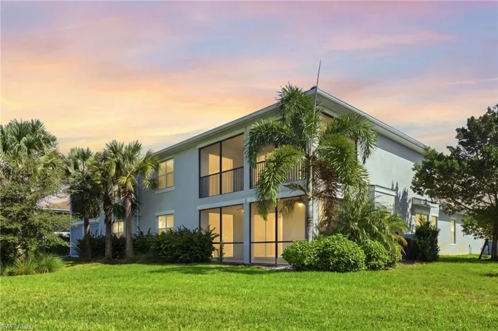 Two-story exterior with light-toned stucco siding, screened balconies, and mature landscaping