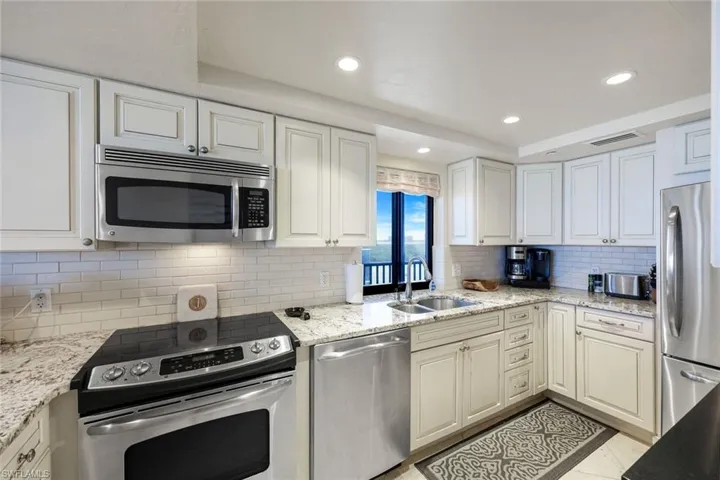 Kitchen featuring stainless steel appliances, tasteful backsplash, light stone countertops, recessed lighting, and white cabinetry