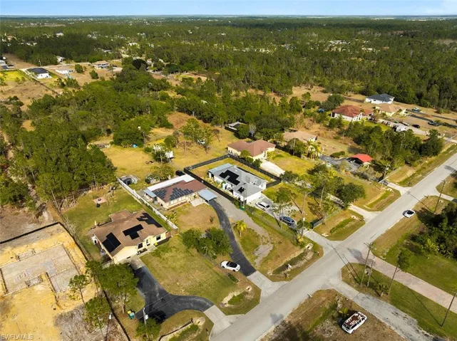 Aerial view of property and surrounding area featuring nearby suburban area and a heavily wooded area