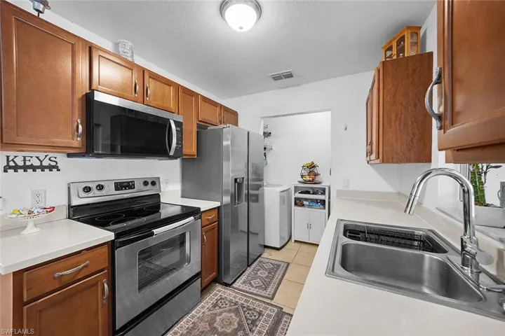 Kitchen with stainless steel appliances, brown cabinets, light countertops, light tile patterned floors, and a textured ceiling