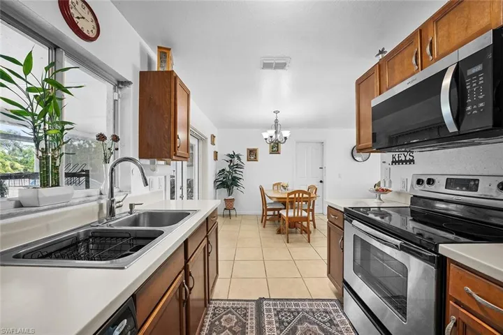 Kitchen featuring appliances with stainless steel finishes, brown cabinetry, decorative light fixtures, light countertops, and light tile patterned flooring