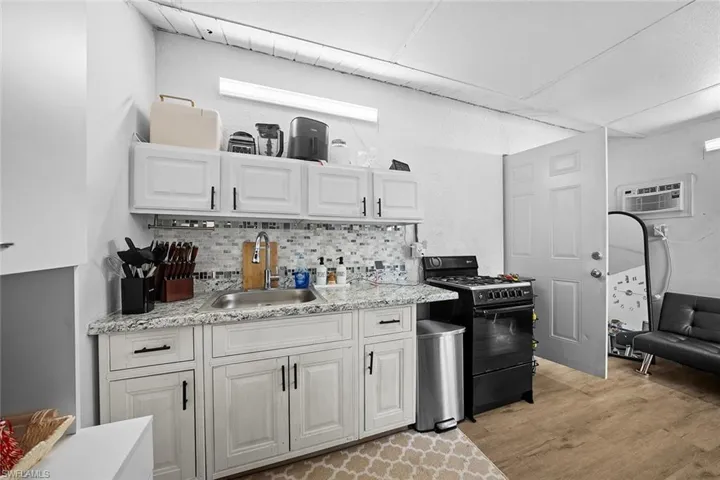 Kitchen with black range with gas stovetop, white cabinetry, light wood-style floors, backsplash, and light stone counters