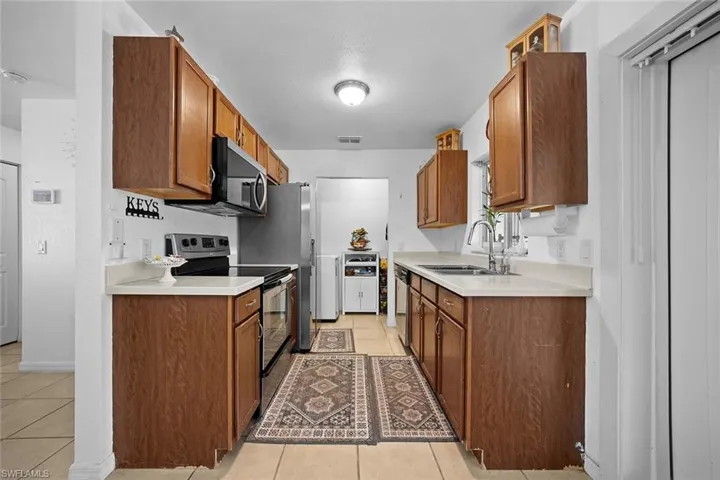 Kitchen featuring appliances with stainless steel finishes, light countertops, light tile patterned floors, and brown cabinetry