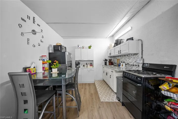 Kitchen with black appliances, white cabinetry, tasteful backsplash, light wood finished floors, and a textured wall
