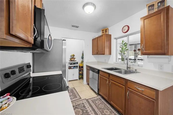 Kitchen with brown cabinetry, appliances with stainless steel finishes, light countertops, and light tile patterned floors