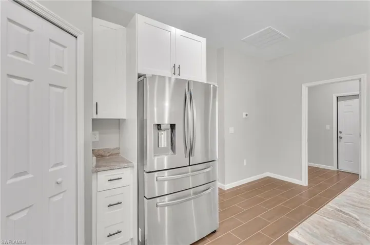 Kitchen featuring stainless steel fridge with ice dispenser, visible vents, baseboards, white cabinetry, and light stone counters