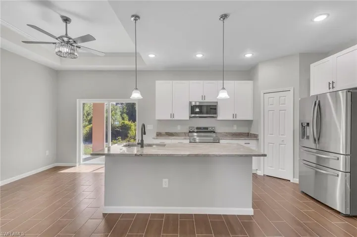 Kitchen with baseboards, dark wood-style floors, a ceiling fan, appliances with stainless steel finishes, and a sink