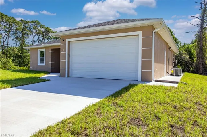 View of front of home with concrete driveway, stucco siding, cooling unit, and a front lawn