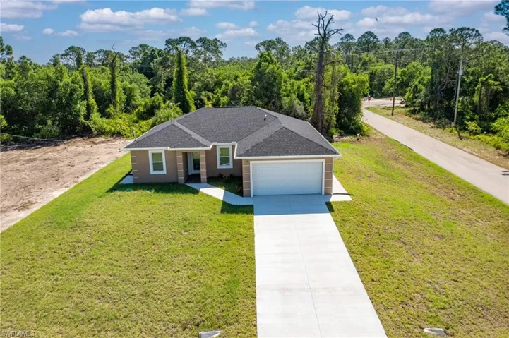 View of front of property with concrete driveway, a front yard, a forest view, a garage, and a shingled roof