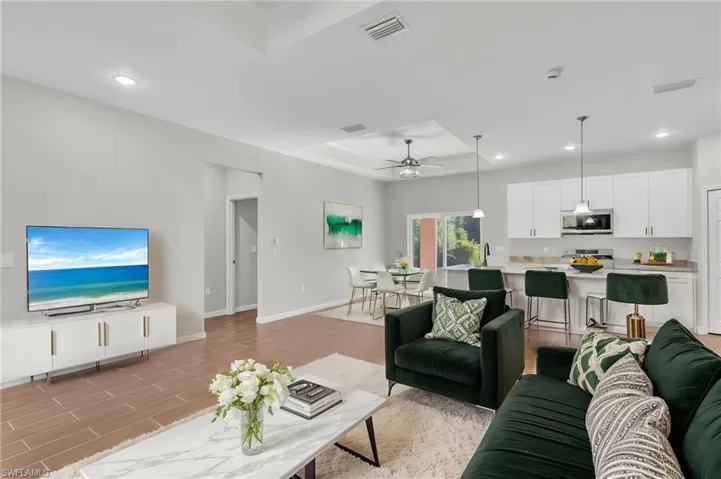 Living area with visible vents, baseboards, a raised ceiling, and recessed lighting