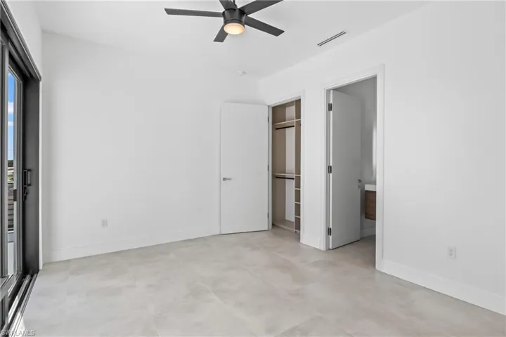 Unfurnished bedroom featuring a ceiling fan, ensuite bath, and concrete flooring