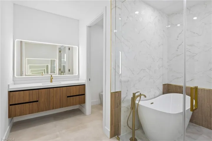 Full bath featuring vanity, tile walls, a soaking tub, and stone wall