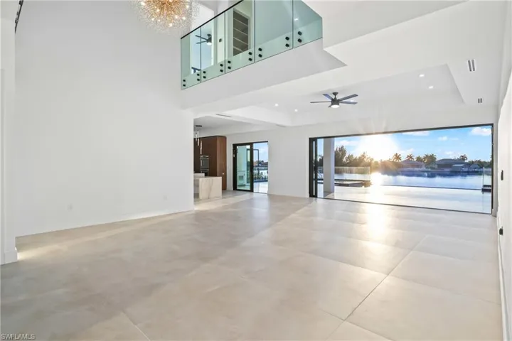 Unfurnished living room featuring a chandelier, a ceiling fan, a high ceiling, a water view, and concrete floors