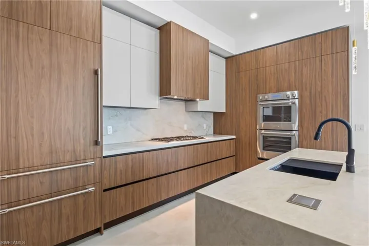 Kitchen with two tone cabinetry, modern cabinets, stainless steel appliances, light stone counters, and backsplash
