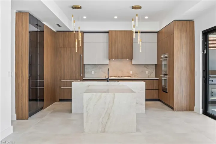 Dual tone kitchen with light stone counters, hanging light fixtures, an island with sink, modern cabinets, and dual tone cabinetry