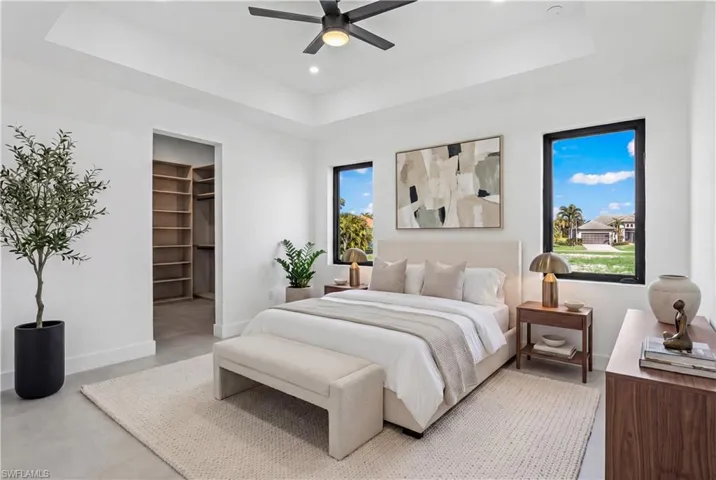 Bedroom featuring a walk in closet, a tray ceiling, finished concrete flooring, ceiling fan, and recessed lighting