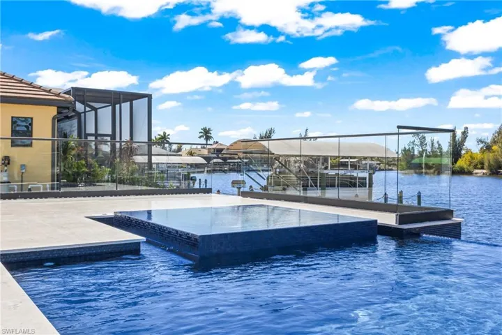 View of pool featuring a dock, glass enclosure, an infinity pool, and boat lift