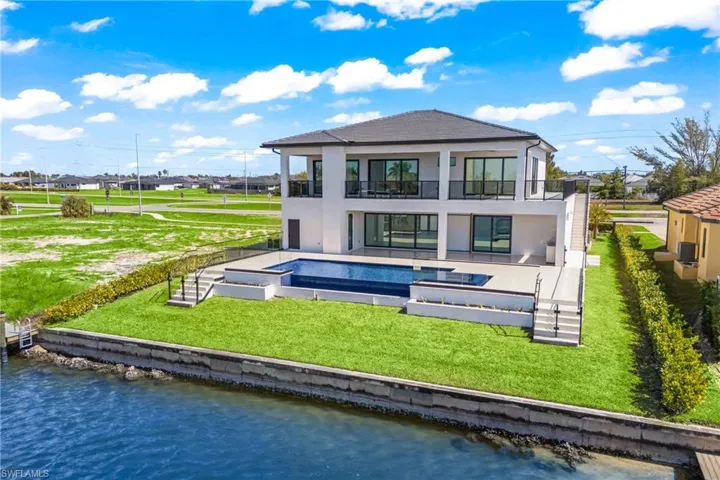 Back of house with a patio area, stucco siding, a balcony, an outdoor pool, and a water view