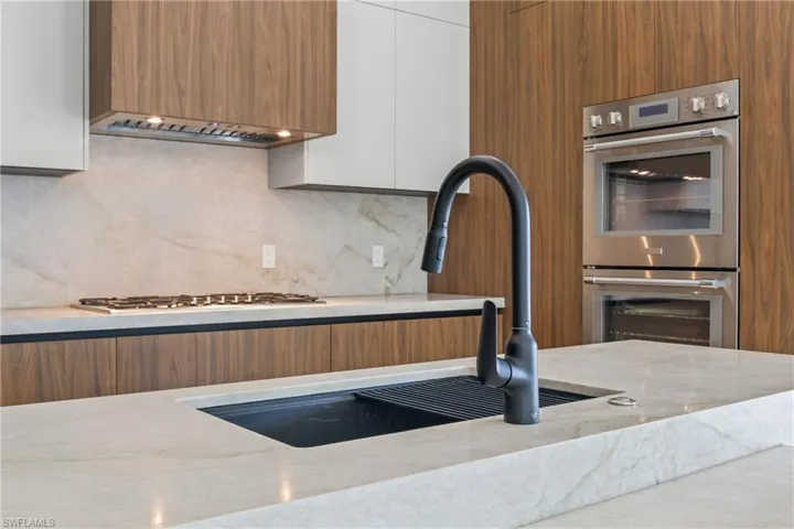 Kitchen featuring modern cabinets, stainless steel double oven, light stone countertops, two tone cabinets, and decorative backsplash