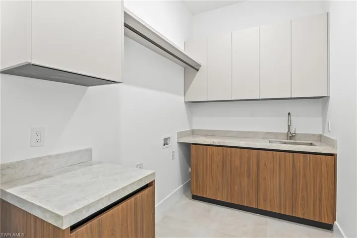 Laundry area featuring hookup for a washing machine, bar with sink, light tile patterned flooring, and cabinet space