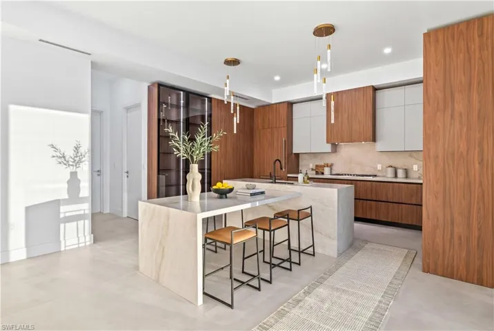 Kitchen featuring two tone cabinetry, modern cabinets, a breakfast bar area, a center island with sink, and decorative light fixtures