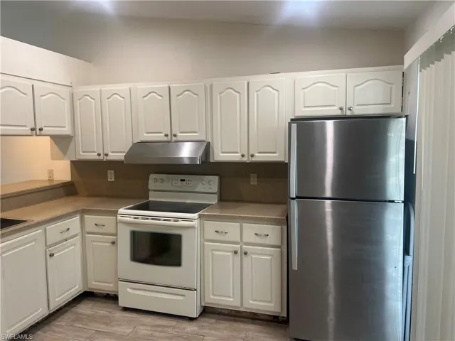Kitchen with white electric range, freestanding refrigerator, white cabinetry, under cabinet range hood, and light wood-style floors