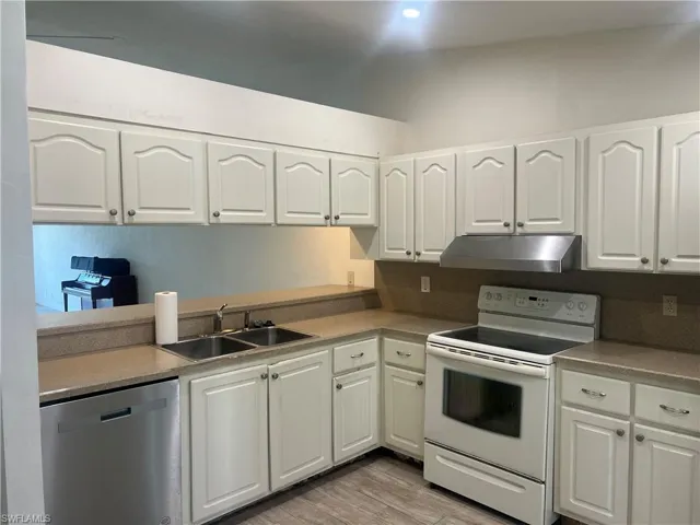 Kitchen featuring electric range, stainless steel dishwasher, white cabinetry, under cabinet range hood, and light countertops