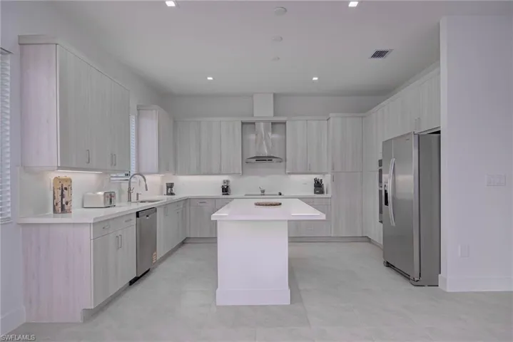 Kitchen with stainless steel appliances, wall chimney exhaust hood, a kitchen island, modern cabinets, and recessed lighting