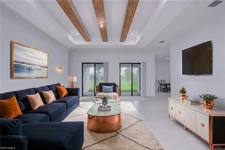 Living room featuring recessed lighting, finished concrete flooring, beamed ceiling, and a tray ceiling- digitally staged