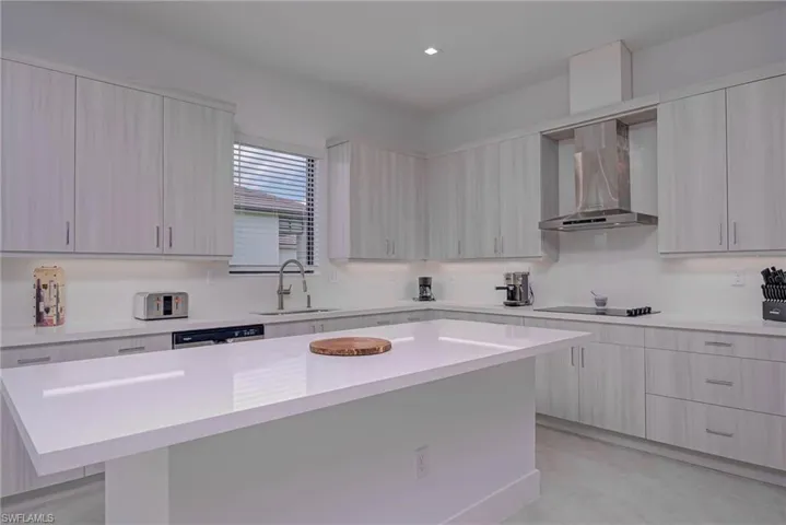 Kitchen with wall chimney exhaust hood, light countertops, modern cabinets, stainless steel dishwasher, and a kitchen island