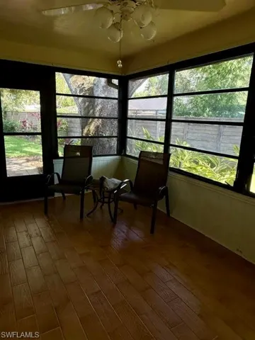 Sunroom featuring wood-finish flooring, a wall of windows, and a ceiling fan with integrated lighting
