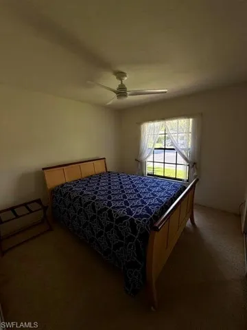 Carpeted room with a ceiling fan, a window with sheer white curtains, and neutral-toned walls