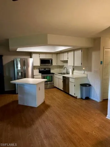 Kitchen with wood-finish flooring, white cabinetry, stainless steel appliances, and a central island