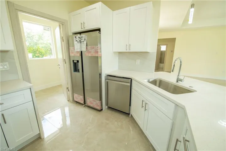 Kitchen featuring stainless steel appliances, white cabinets, light stone countertops, and hanging light fixtures
