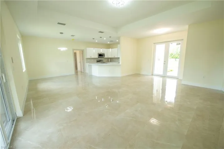 Unfurnished living room featuring french doors, a tray ceiling, recessed lighting, and light marble finish floors