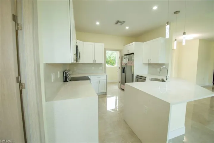 Kitchen with a peninsula, light stone countertops, stainless steel appliances, white cabinetry, and hanging light fixtures