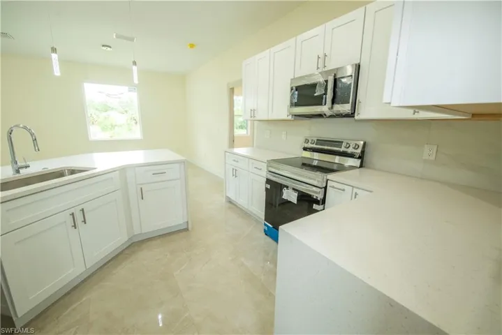 Kitchen featuring stainless steel appliances, white cabinets, light stone countertops, and hanging light fixtures