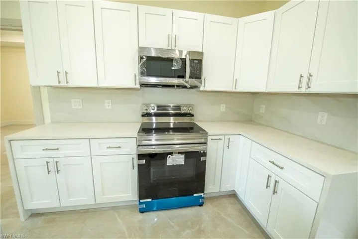 Kitchen with stainless steel appliances, white cabinetry, light stone countertops, and decorative backsplash