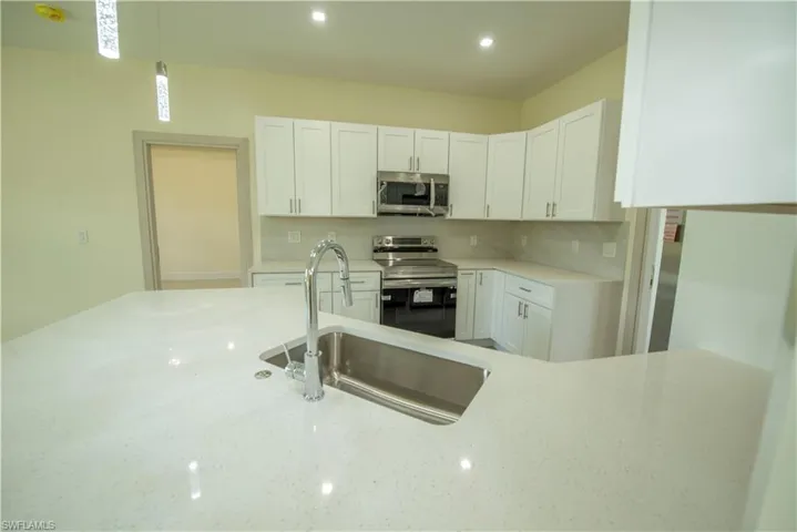 Kitchen featuring white cabinets, stainless steel appliances, light stone countertops, pendant lighting, and decorative backsplash