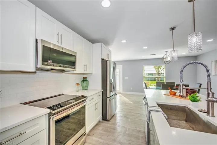 Kitchen with sink, decorative light fixtures, white cabinets, light wood-type flooring, and appliances with stainless steel finishes