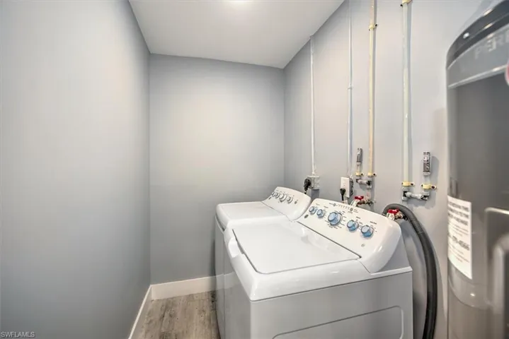 Laundry area featuring washer and dryer, strapped water heater, and hardwood / wood-style floors