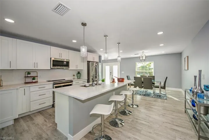 Kitchen with a center island with sink, decorative light fixtures, white cabinetry, and appliances with stainless steel finishes