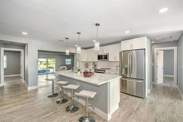 Kitchen featuring a kitchen breakfast bar, stainless steel appliances, an island with sink, pendant lighting, and white cabinets